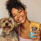 Woman holding a dog and a package of probiotics for dogs supplement in a pouch, smiling at the camera.